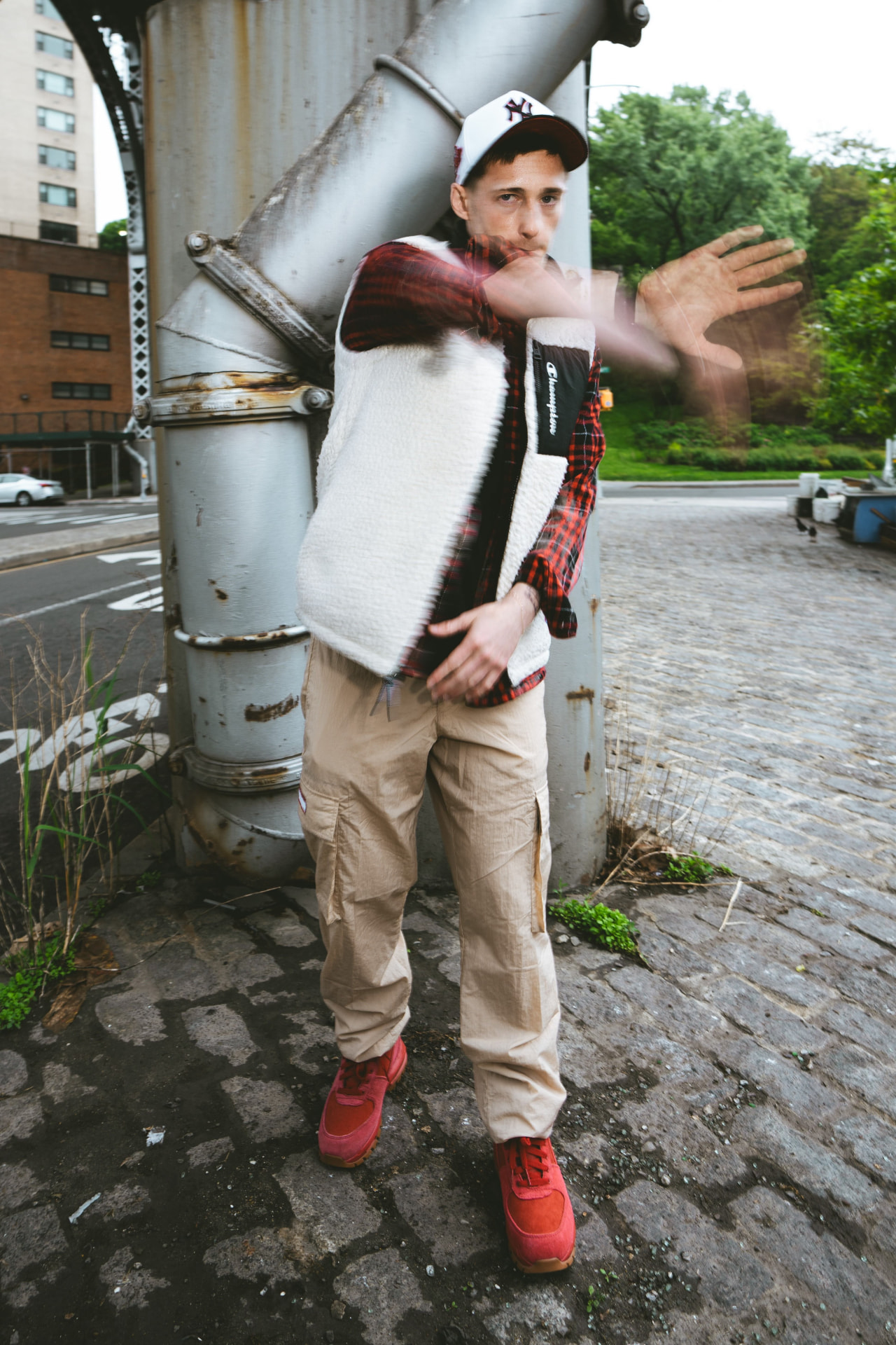 Kaden Quinn in a Yankees cap and flannel with a motion-blurred hand sweeping across the frame on a cobblestone street