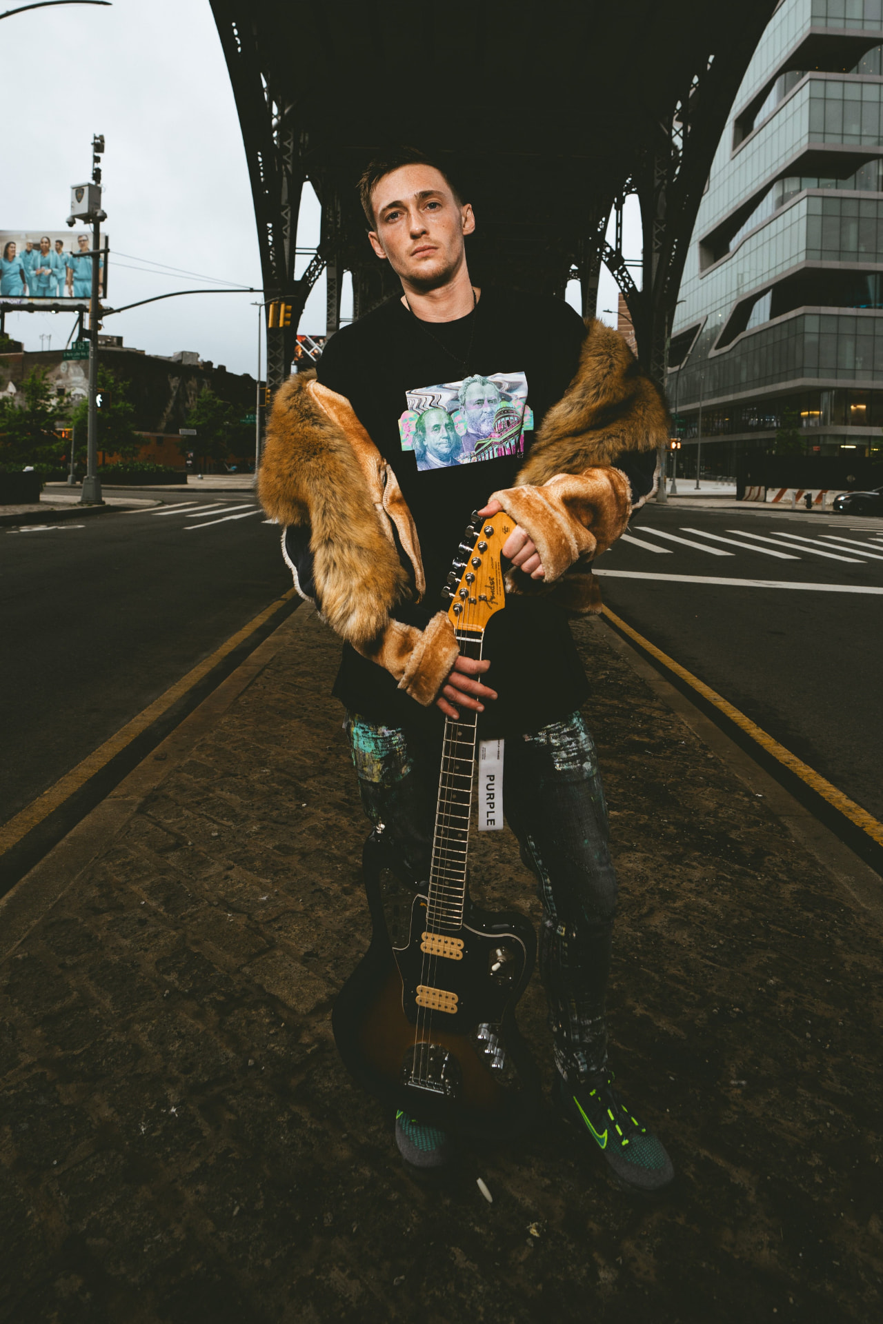 Kaden Quinn standing under the 125th Street elevated subway arch in Harlem holding an electric guitar