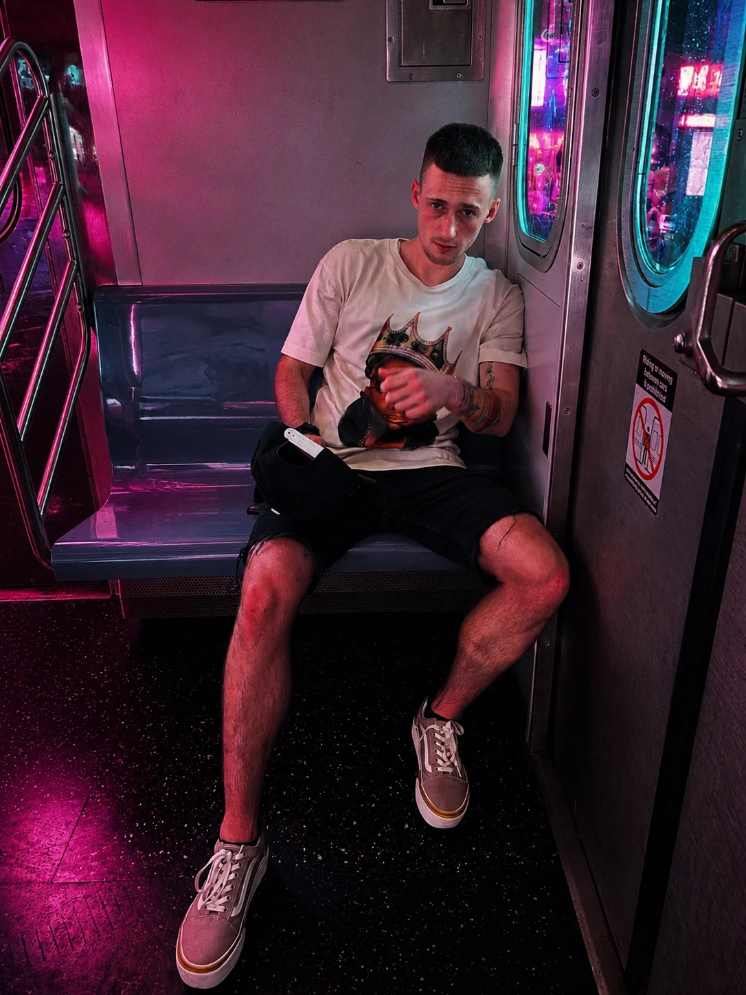 Kaden Quinn seated on an NYC subway train in a Biggie Smalls graphic tee under pink neon light